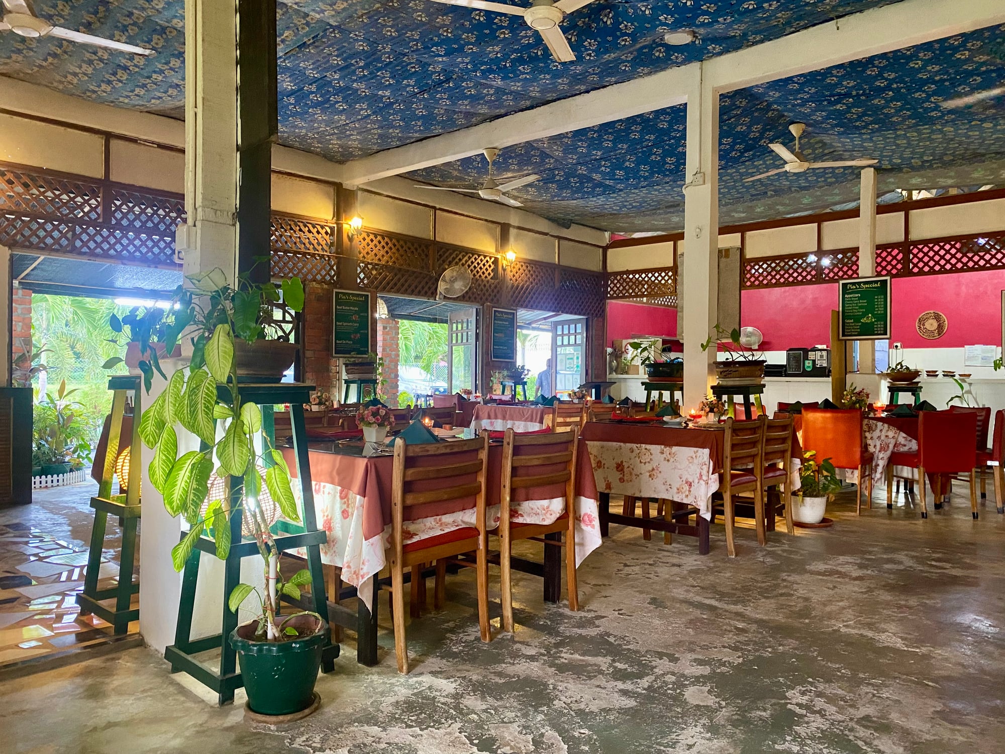The open dining room at Pia's the Padi: long tables under a printed indigo ceiling, wooden lattice screens, and greenery through the open sides.