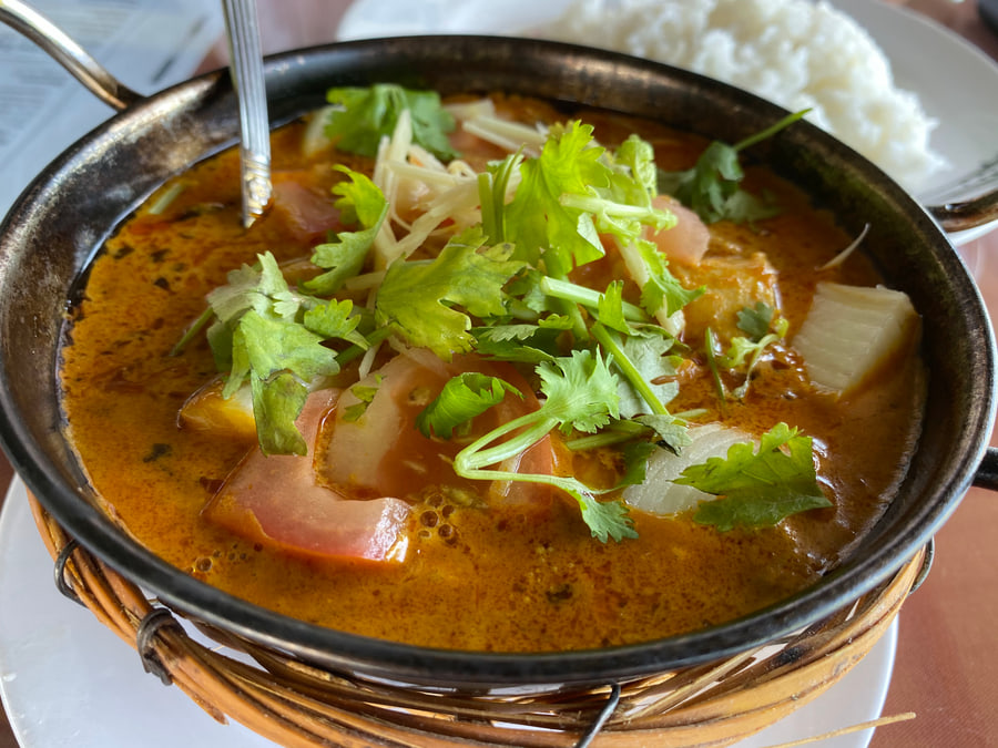 Masala in a black karahi with coriander and tomato on top, a bowl of steamed rice beside it.
